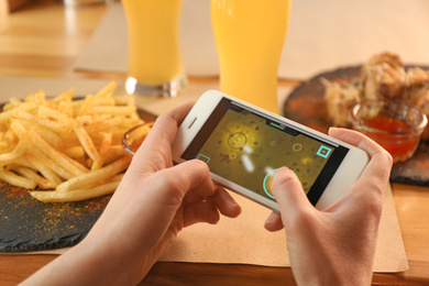 Woman playing game using smartphone at table with tasty snacks, closeup Photo of Woman playing game using smartphone at table with tasty snacks, closeup