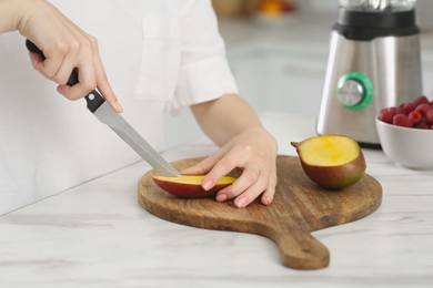 Woman preparing mango for tasty smoothie at white marble table in kitchen, closeup Photo of Woman preparing mango for tasty smoothie at white marble table in kitchen, closeup