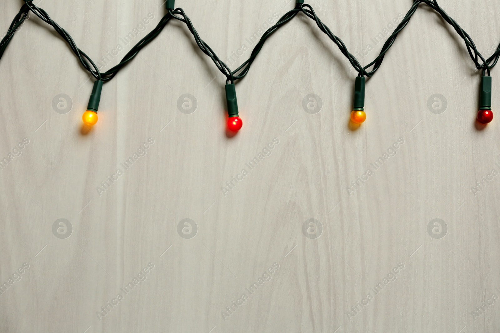 Beautiful glowing Christmas lights on white wooden background, top view. Space for text Photo of Beautiful glowing Christmas lights on white wooden background, top view. Space for text