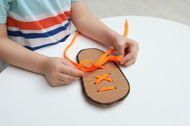 Little boy tying shoe lace using training cardboard template at white table, closeup Photo of Little boy tying shoe lace using training cardboard template at white table, closeup