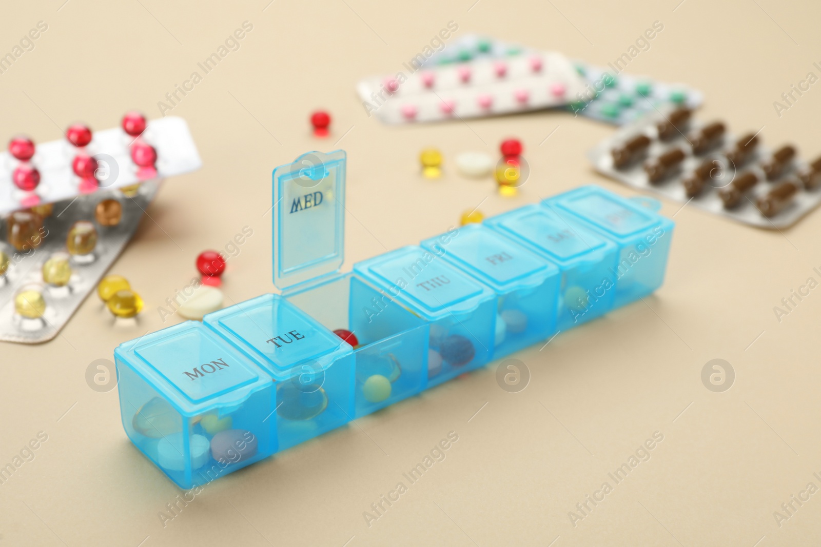 Plastic box with different pills on beige background Photo of Plastic box with different pills on beige background