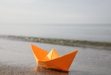 Orange paper boat on sandy beach near sea, space for text Photo of Orange paper boat on sandy beach near sea, space for text