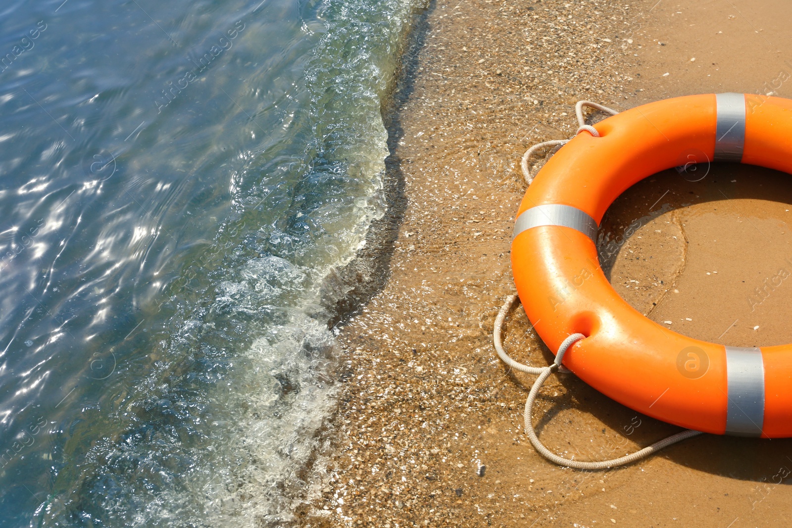 Orange life buoy on sand near sea, closeup. Emergency rescue equipment Photo of Orange life buoy on sand near sea, closeup. Emergency rescue equipment