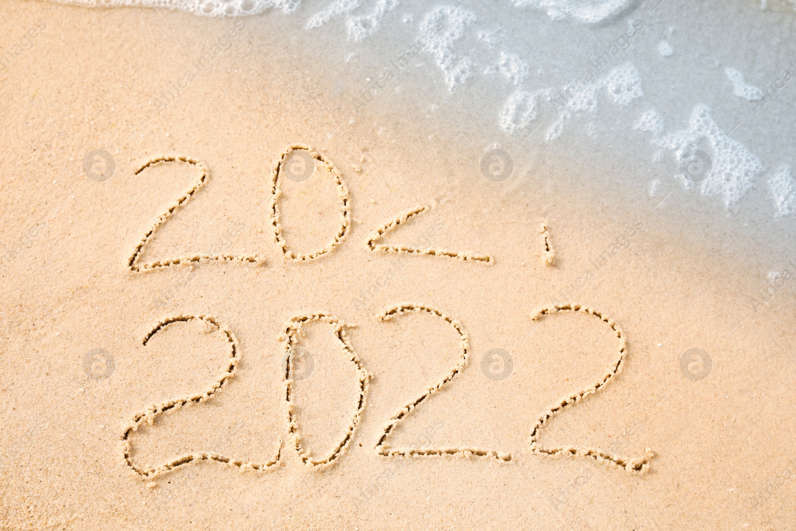 Dates written on sandy beach. 2021 washed by sea wave as New 2022 Year coming, above view Photo of Dates written on sandy beach. 2021 washed by sea wave as New 2022 Year coming, above view