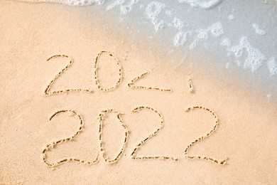 Dates written on sandy beach. 2021 washed by sea wave as New 2022 Year coming, above view Photo of Dates written on sandy beach. 2021 washed by sea wave as New 2022 Year coming, above view