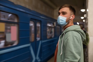 Young man in protective mask at subway station, space for text. Public transport Photo of Young man in protective mask at subway station, space for text. Public transport
