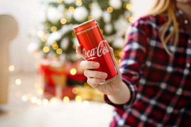 MYKOLAIV, UKRAINE - January 01, 2021: Woman with can of Coca-Cola against blurred Christmas tree indoors, closeup Photo of MYKOLAIV, UKRAINE - January 01, 2021: Woman with can of Coca-Cola against blurred Christmas tree indoors, closeup