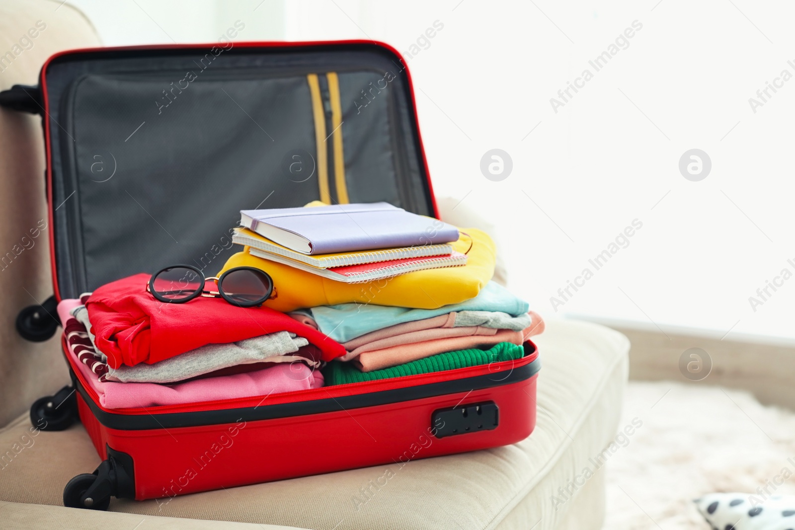 Travel suitcase with clothes and notebooks on sofa Photo of Travel suitcase with clothes and notebooks on sofa