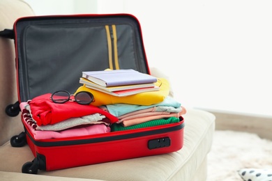 Travel suitcase with clothes and notebooks on sofa Photo of Travel suitcase with clothes and notebooks on sofa