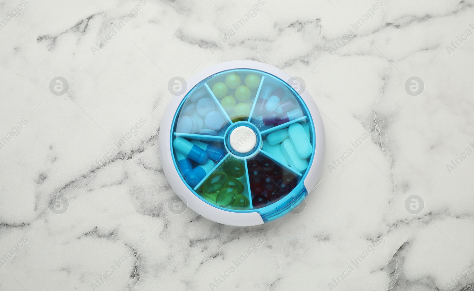 Photo of Plastic box with different pills on white marble table, top view
