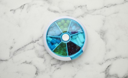 Plastic box with different pills on white marble table, top view Photo of Plastic box with different pills on white marble table, top view