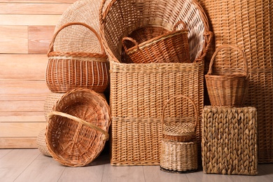 Many different wicker baskets made of natural material on floor near wooden wall Photo of Many different wicker baskets made of natural material on floor near wooden wall