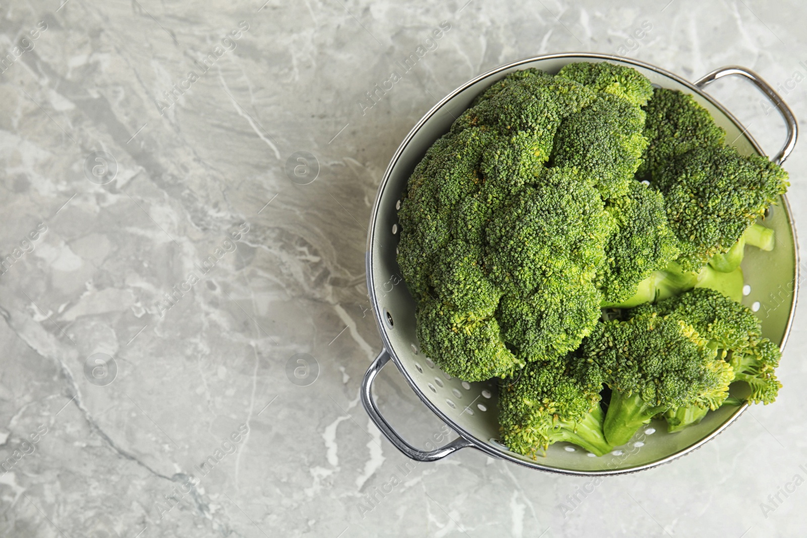 Fresh green broccoli in colander on grey marble table, top view. Space for text Photo of Fresh green broccoli in colander on grey marble table, top view. Space for text