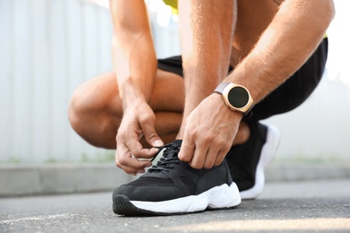 Man with fitness tracker tying shoelaces outdoors, closeup Photo of Man with fitness tracker tying shoelaces outdoors, closeup