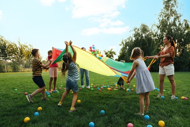 Group of children and teacher playing with rainbow playground parachute on green grass. Summer camp activity Photo of Group of children and teacher playing with rainbow playground parachute on green grass. Summer camp activity