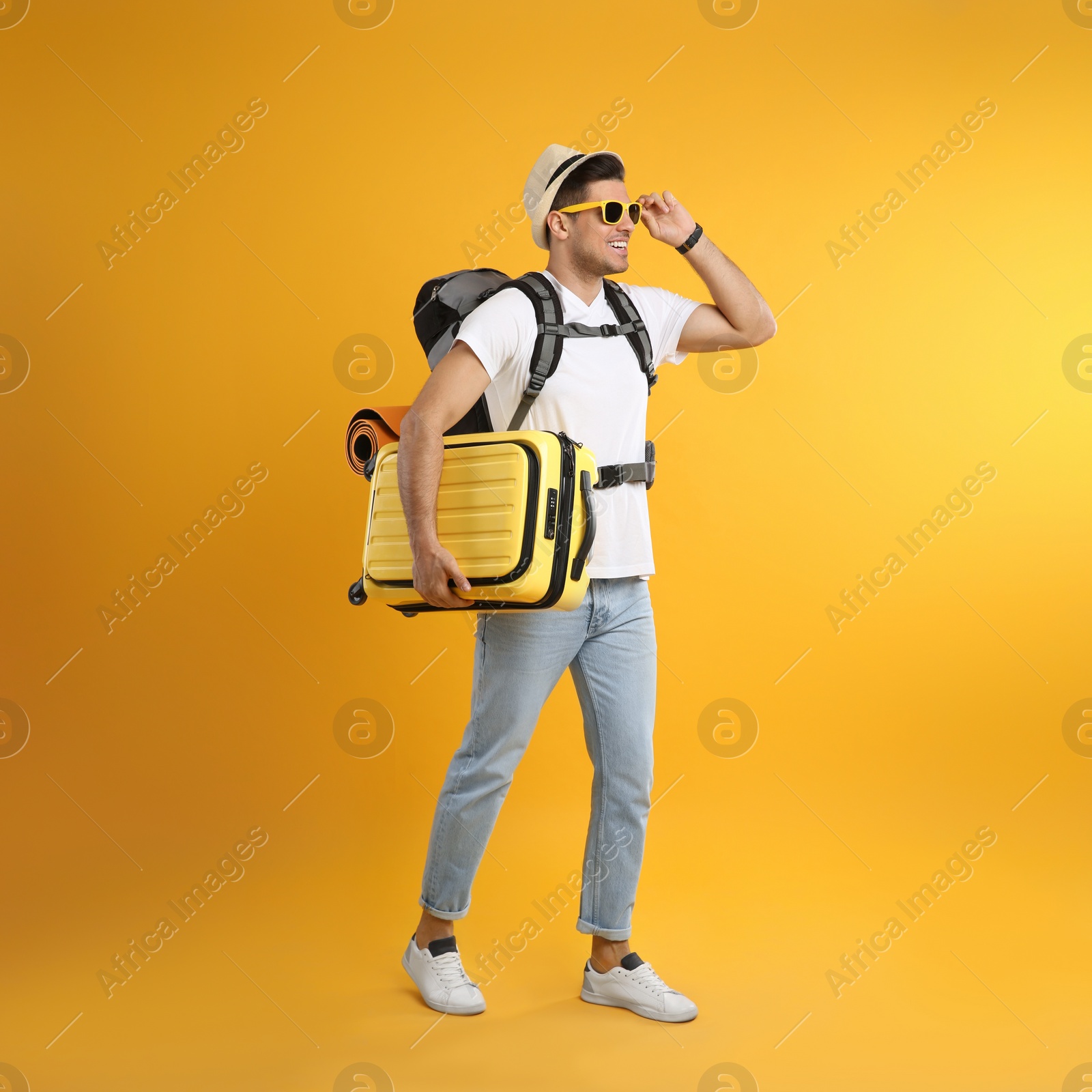 Male tourist with travel backpack and suitcase on yellow background Photo of Male tourist with travel backpack and suitcase on yellow background