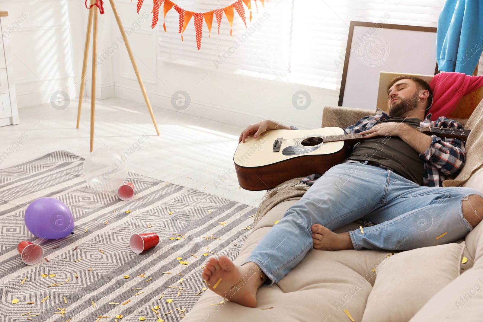 Young man with guitar sleeping on sofa in messy room after party Photo of Young man with guitar sleeping on sofa in messy room after party