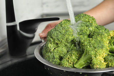 Woman washing fresh green broccoli in kitchen sink, closeup Photo of Woman washing fresh green broccoli in kitchen sink, closeup