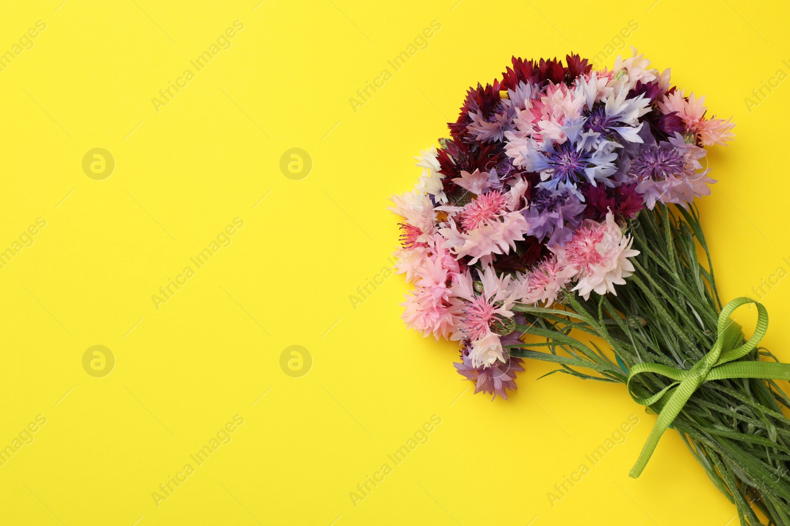 Bouquet of beautiful colorful cornflowers on yellow background, top view. Space for text Photo of Bouquet of beautiful colorful cornflowers on yellow background, top view. Space for text