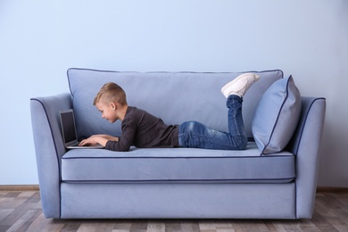 Cute little boy lying on sofa with laptop, indoors Photo of Cute little boy lying on sofa with laptop, indoors