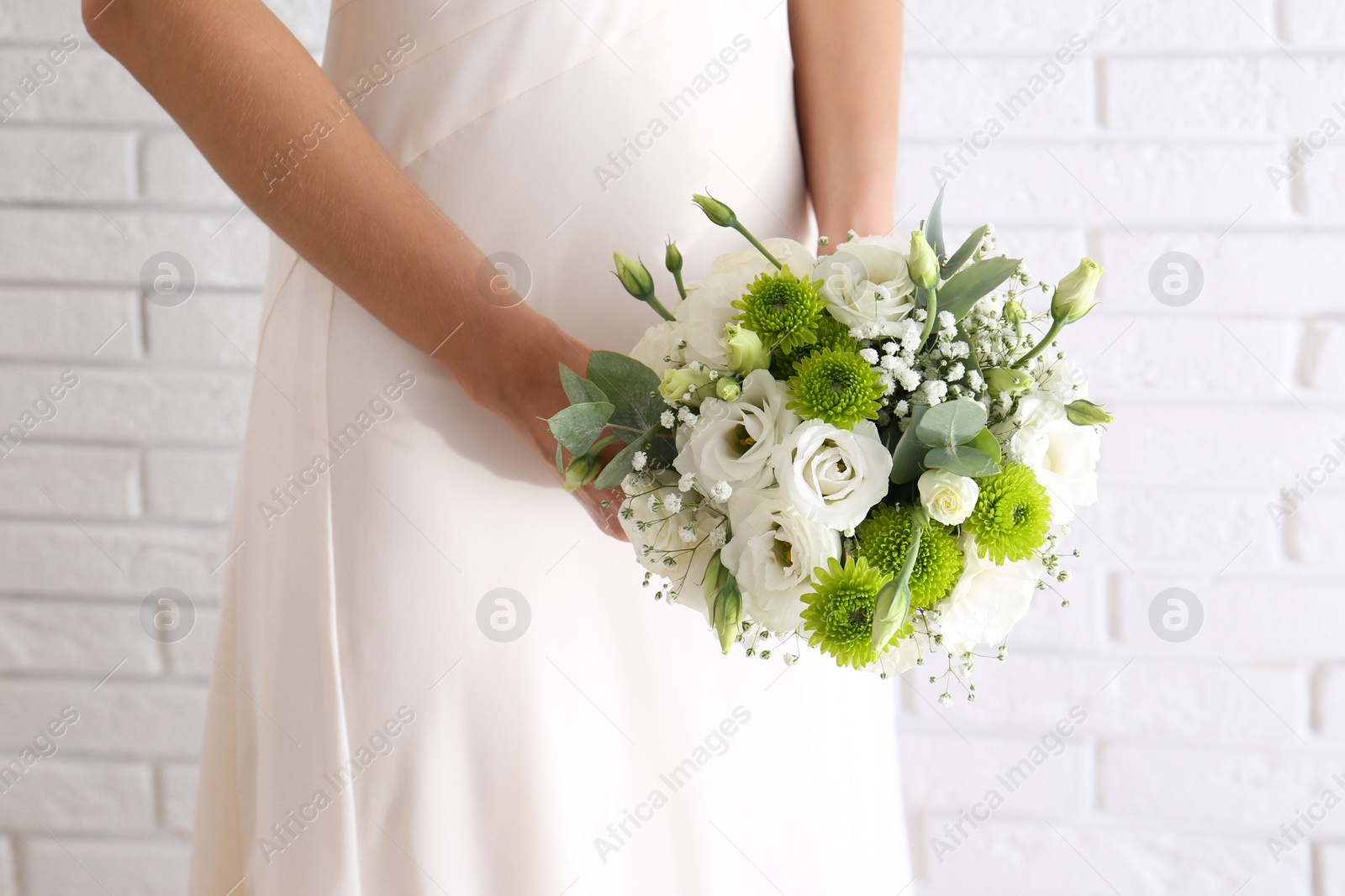 Bride holding beautiful bouquet with Eustoma flowers near brick wall, closeup Photo of Bride holding beautiful bouquet with Eustoma flowers near brick wall, closeup