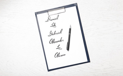 Clipboard with written different baby names and pen on white wooden table, top view Photo of Clipboard with written different baby names and pen on white wooden table, top view