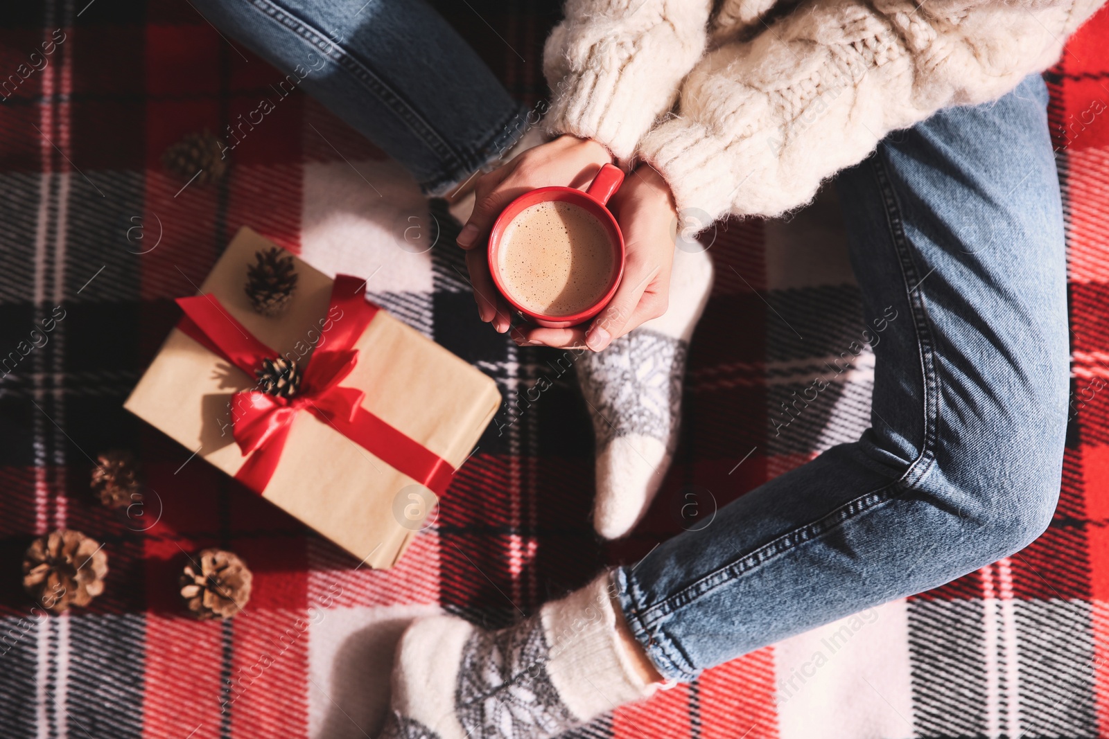 Photo of Woman relaxing with cup of hot winter drink on checkered plaid, top view