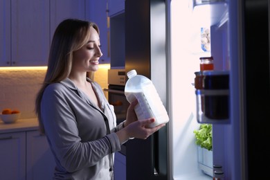 Young woman holding gallon bottle of milk near refrigerator in kitchen at night Photo of Young woman holding gallon bottle of milk near refrigerator in kitchen at night