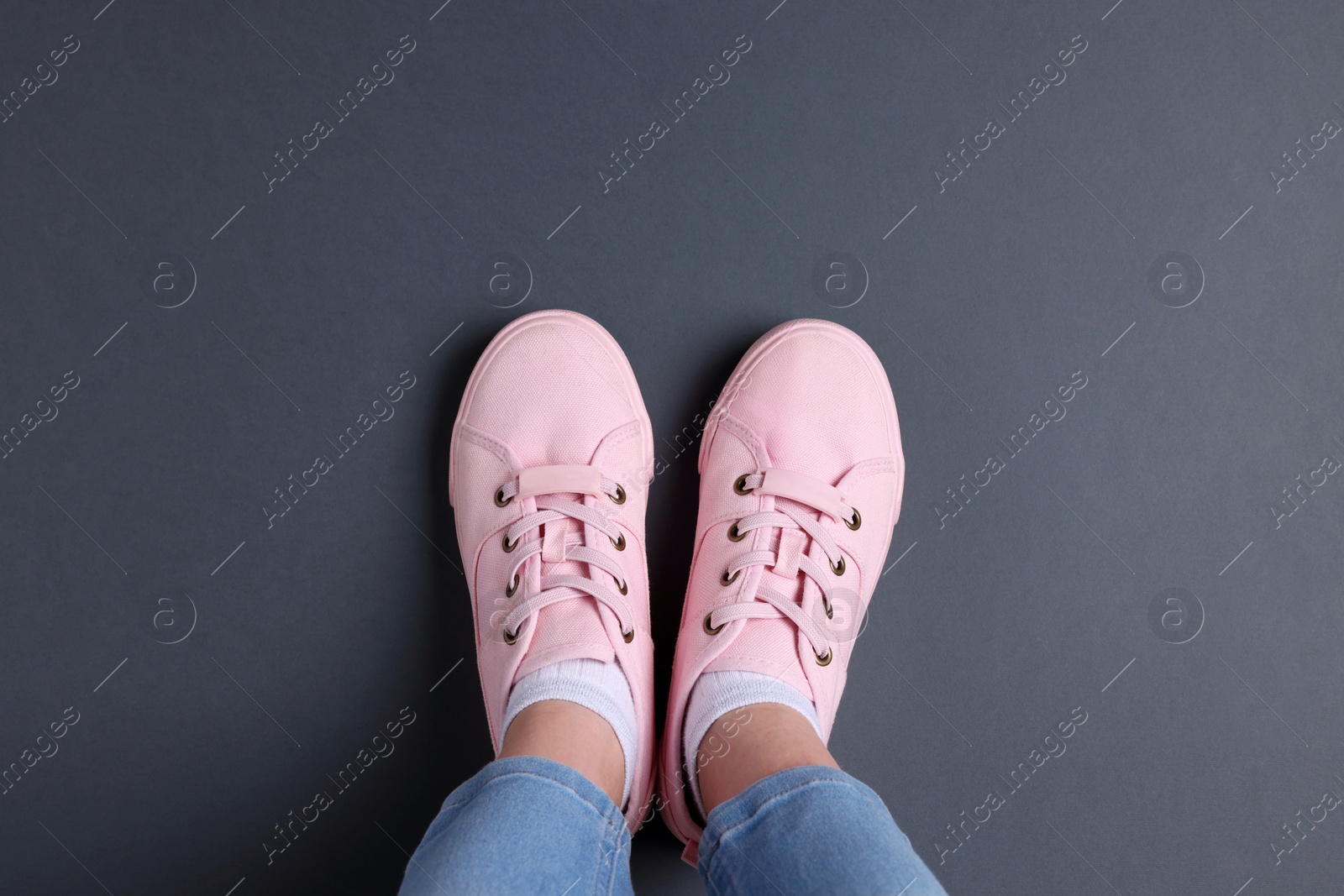Woman in stylish sneakers standing on grey background. Space for text Photo of Woman in stylish sneakers standing on grey background. Space for text