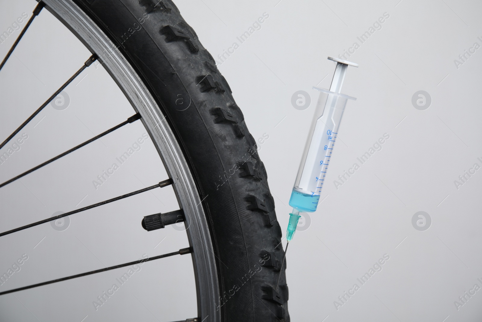 Bike wheel with syringe on light background, closeup. Using doping in cycling sport concept Photo of Bike wheel with syringe on light background, closeup. Using doping in cycling sport concept