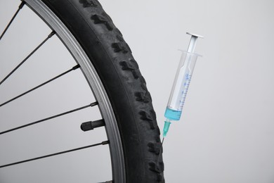 Bike wheel with syringe on light background, closeup. Using doping in cycling sport concept Photo of Bike wheel with syringe on light background, closeup. Using doping in cycling sport concept