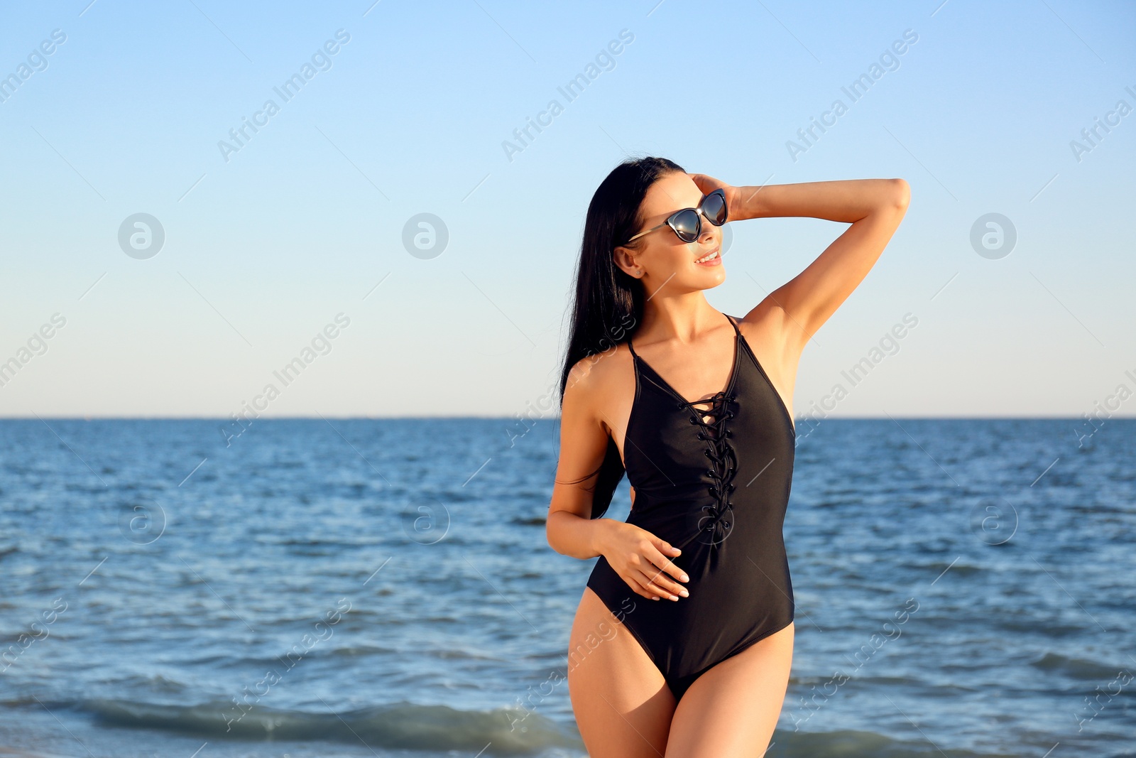 Photo of Beautiful young woman in black stylish swimsuit on beach. Space for text
