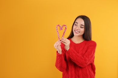 Young woman in red sweater holding candy canes on yellow background, space for text. Celebrating Christmas Photo of Young woman in red sweater holding candy canes on yellow background, space for text. Celebrating Christmas