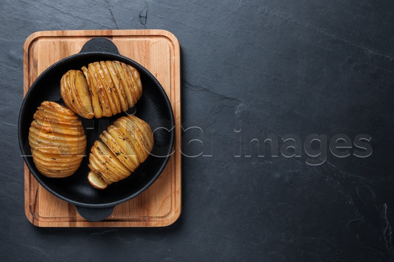 Photo of Delicious homemade Hasselback potatoes on black table, top view. Space for text