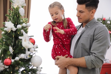 Father with his cute daughter decorating Christmas tree together at home Photo of Father with his cute daughter decorating Christmas tree together at home