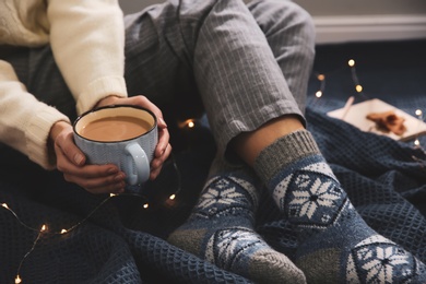 Woman relaxing with cup of hot winter drink on warm plaid indoors, closeup. Cozy season Photo of Woman relaxing with cup of hot winter drink on warm plaid indoors, closeup. Cozy season