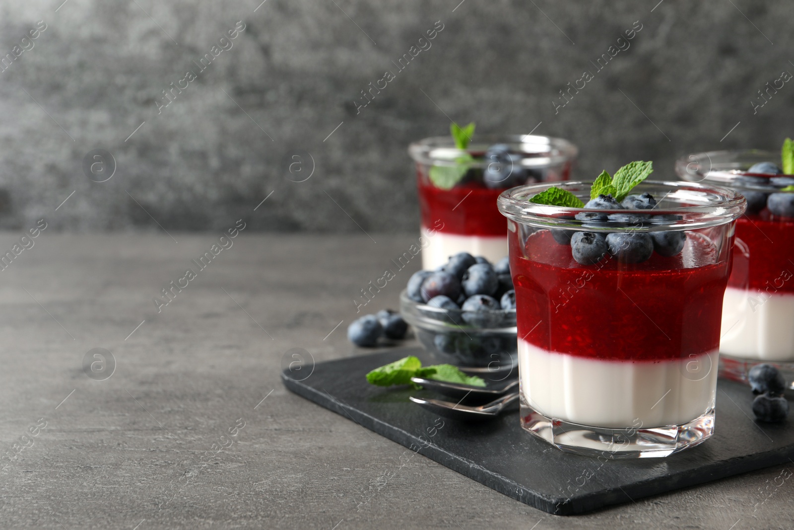 Delicious panna cotta with fruit coulis and fresh blueberries served on grey table. Space for text Photo of Delicious panna cotta with fruit coulis and fresh blueberries served on grey table. Space for text