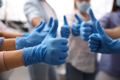 Photo of Group of people in blue medical gloves showing thumbs up on blurred background, closeup