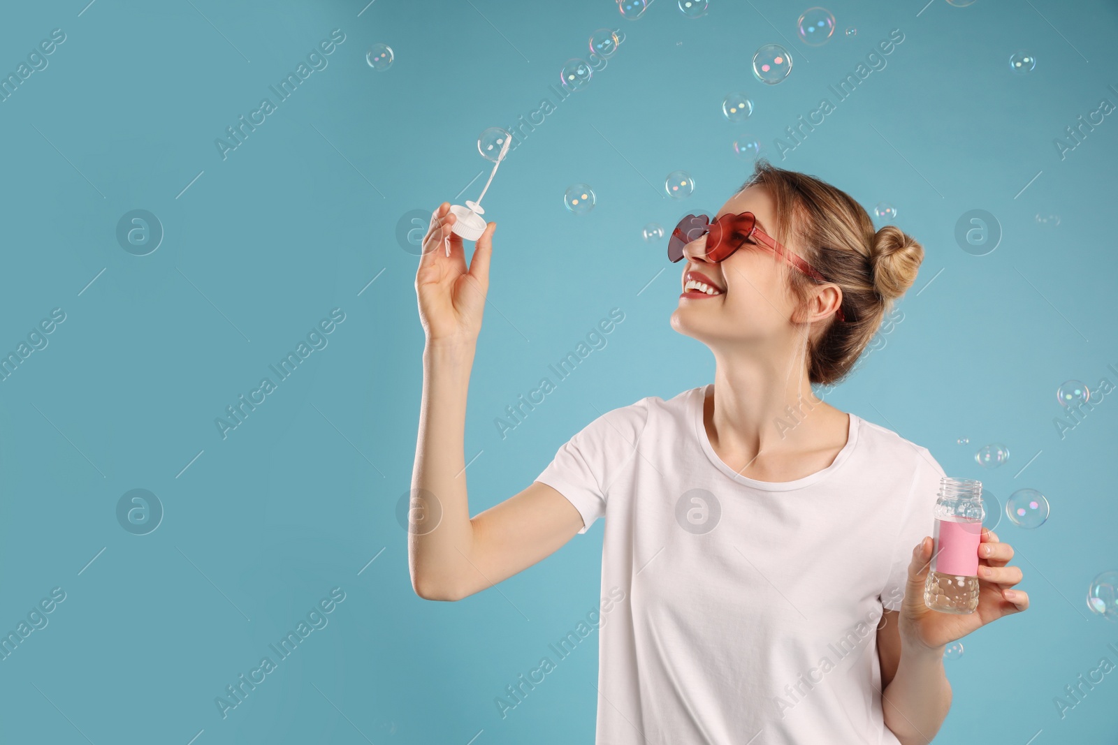 Young woman blowing soap bubbles on light blue background, space for text Photo of Young woman blowing soap bubbles on light blue background, space for text