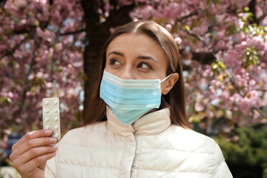 Woman with pills and protective mask near blossoming tree outdoors. Seasonal pollen allergy Photo of Woman with pills and protective mask near blossoming tree outdoors. Seasonal pollen allergy
