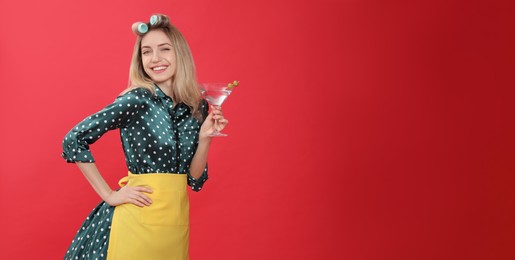 Young housewife with glass of martini on red background. Space for text Photo of Young housewife with glass of martini on red background. Space for text