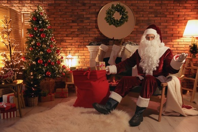 Santa Claus with sack of gifts in armchair at home Photo of Santa Claus with sack of gifts in armchair at home