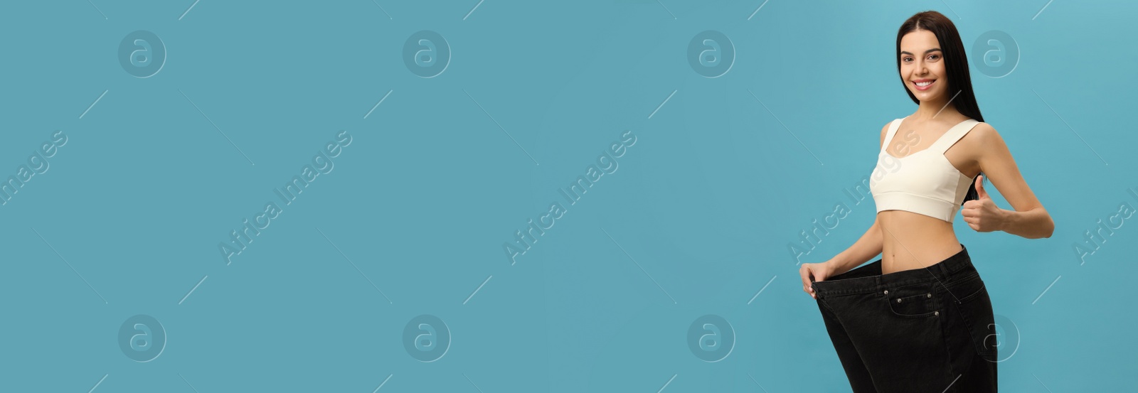 Happy young woman wearing big jeans after weight loss on turquoise background Photo of Happy young woman wearing big jeans after weight loss on turquoise background