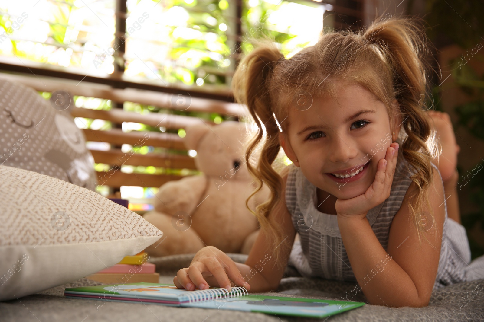 Cute little girl reading book near window at home Photo of Cute little girl reading book near window at home