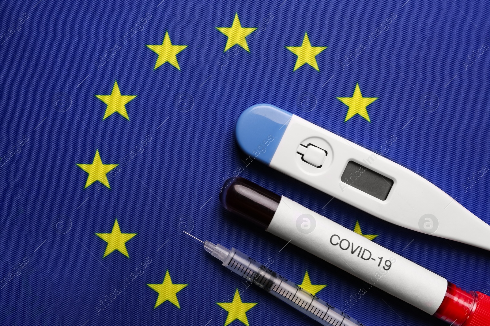 Test tube with blood sample, thermometer and syringe on European Union flag background, flat lay. Coronavirus outbreak Photo of Test tube with blood sample, thermometer and syringe on European Union flag background, flat lay. Coronavirus outbreak