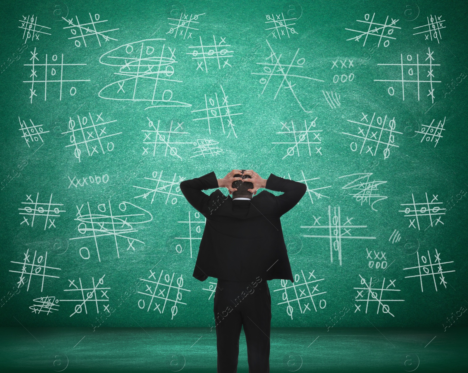 Young businessman near green chalkboard with drawn tic tac toe game, back view Image of Young businessman near green chalkboard with drawn tic tac toe game, back view