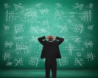Young businessman near green chalkboard with drawn tic tac toe game, back view Image of Young businessman near green chalkboard with drawn tic tac toe game, back view