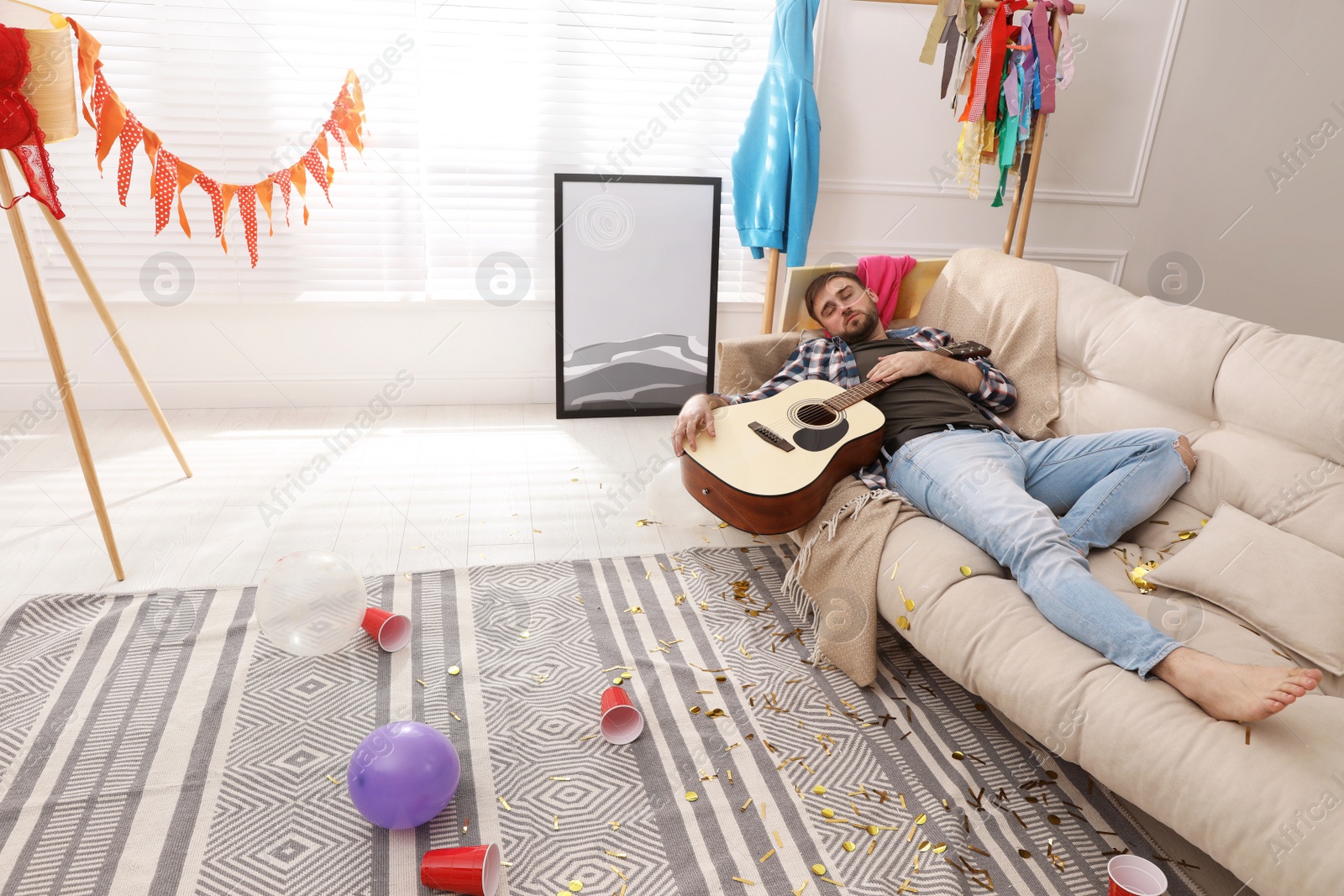 Young man with guitar sleeping on sofa in messy room after party Photo of Young man with guitar sleeping on sofa in messy room after party