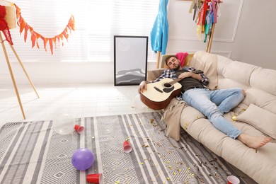 Young man with guitar sleeping on sofa in messy room after party Photo of Young man with guitar sleeping on sofa in messy room after party