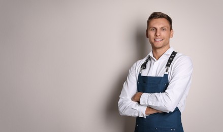 Portrait of happy young waiter in uniform on light background Photo of Portrait of happy young waiter in uniform on light background